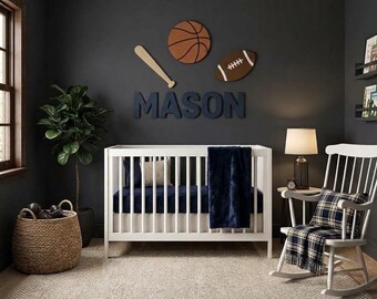 Könnte beinhalten: Ein weißes Gitterbett mit einer dunkelblauen Decke und Bettwäsche vor einer dunkelgrauen Wand, die mit Holzdekorationen in Form eines Basketballs, eines Footballs, eines Baseballschlägers und dem Namen MASON in großen Buchstaben verziert ist.
