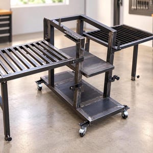 May include: A dark gray industrial metal workstation featuring a central vertical frame with multiple shelves, two side extensions with slatted surfaces, and a base supported by four swivel caster wheels for mobility in a workshop environment.