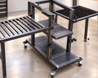 May include: A dark gray industrial metal workstation featuring a central vertical frame with multiple shelves, two side extensions with slatted surfaces, and a base supported by four swivel caster wheels for mobility in a workshop environment.