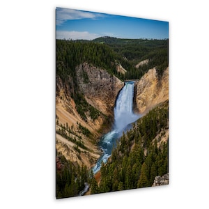 Könnte beinhalten: Ein vertikaler Wandkunstdruck mit einer Ansicht von oben auf einen mächtigen Wasserfall, der in eine tiefe Schlucht stürzt. Das Bild zeigt zerklüftete, ockerfarbene und orangefarbene Felsklippen, dichte Kiefernwälder und einen hellblauen Himmel.