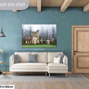 Op de afbeelding: Een wandprint met een stenen kasteel in een mistig bos, weergegeven boven een cr&egrave;mekleurige hoekbank. De tekst Livingroom size chart is bovenaan zichtbaar, met 40x60in | 101x152cm in de linkerbenedenhoek.