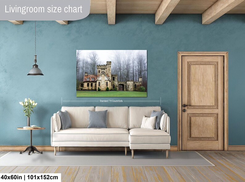 Op de afbeelding: Een wandprint met een stenen kasteel in een mistig bos, weergegeven boven een cr&egrave;mekleurige hoekbank. De tekst Livingroom size chart is bovenaan zichtbaar, met 40x60in | 101x152cm in de linkerbenedenhoek.