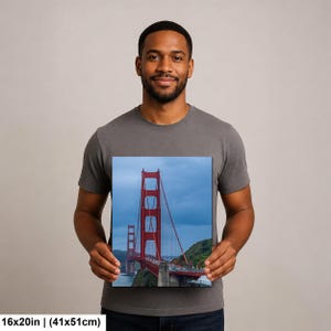 May include: A rectangular wall art print featuring a vertical perspective of the Golden Gate Bridge in San Francisco. The iconic red-orange suspension bridge spans across blue water under a cloudy sky, measuring 16 inches by 20 inches in size.