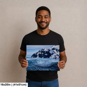 May include: A rectangular wall art print measuring 16 by 20 inches, featuring a landscape photograph of a dark blue, textured glacial ice formation in the foreground with snow-capped mountains under a pale sky in the background.