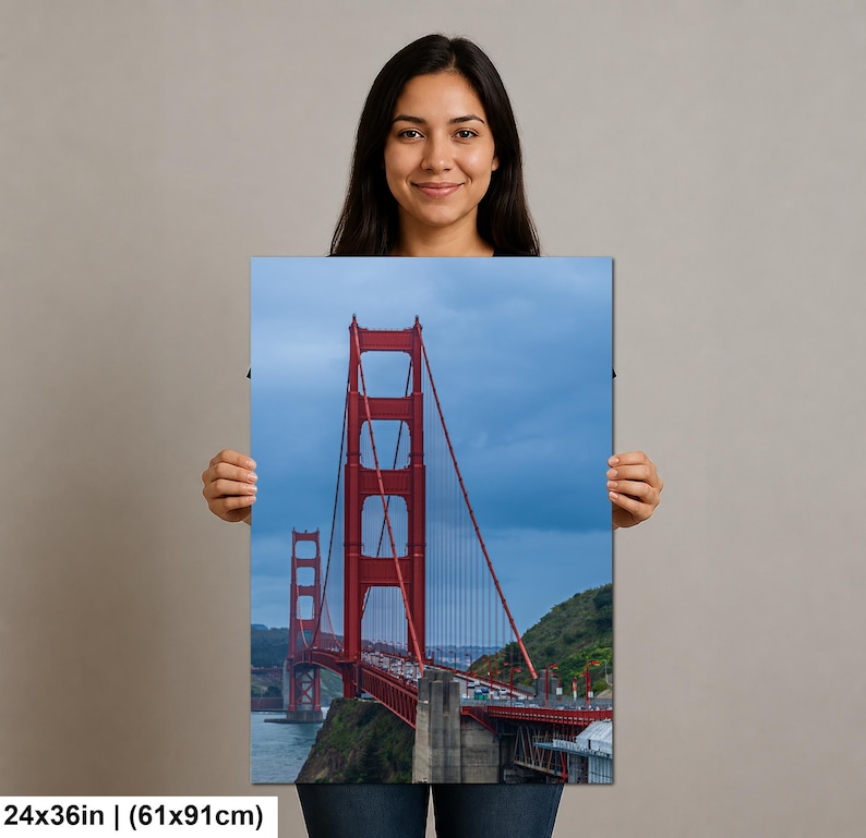 May include: A rectangular wall art print featuring the Golden Gate Bridge in San Francisco, displaying its iconic red-orange towers and suspension cables against a cloudy blue sky, measuring 24 inches by 36 inches in total dimensions.