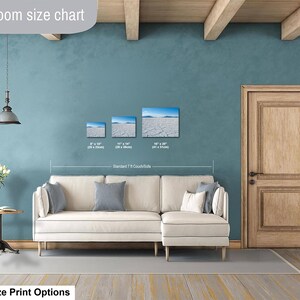 May include: A living room size chart showing three rectangular wall art prints above a cream-colored sectional sofa. The prints display a dry cracked landscape under a blue sky, with sizes labeled as 8x10 inches, 11x14 inches, and 16x20 inches.