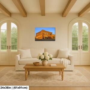 May include: A rectangular wall art print featuring a historic orange brick building under a clear blue sky, displayed in a living room above a white sofa. The print measures 24 inches by 36 inches, showcasing architectural details of the structure.