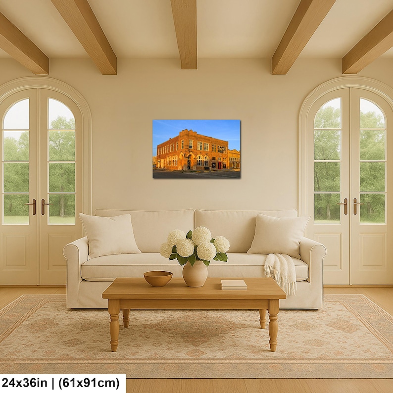 May include: A rectangular wall art print featuring a historic orange brick building under a clear blue sky, displayed in a living room above a white sofa. The print measures 24 inches by 36 inches, showcasing architectural details of the structure.