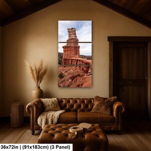 May include: A three-panel wall art set depicting a tall, layered red rock formation under a cloudy sky. The artwork measures 36 by 72 inches and features earthy tones of terracotta, rust, and brown, capturing the rugged texture of the canyon landscape.