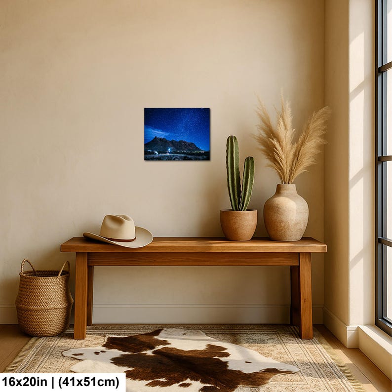 Puede incluir: Una impresi&oacute;n de arte mural rectangular de 41 por 51 cm, que muestra un paisaje nocturno de una cordillera oscura bajo un cielo estrellado azul profundo. La impresi&oacute;n se exhibe en una pared lisa sobre un banco de madera, un sombrero y una cesta.