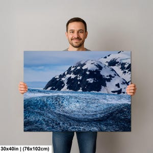 May include: A rectangular wall art print measuring 30 by 40 inches featuring a landscape photograph of a deep blue glacier in the foreground with snow-capped dark mountain peaks rising in the background under a pale blue sky.