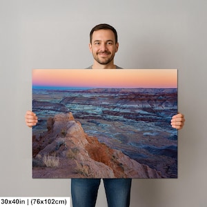 May include: A rectangular landscape wall art print measuring 30 by 40 inches, featuring a desert canyon at sunset with layered rock formations in shades of orange, blue, and grey under a soft pink and orange gradient sky with sparse vegetation.