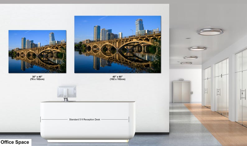 May include: Two rectangular wall art prints featuring a city skyline and a bridge over water. The smaller print is 30 x 40 inches and the larger print is 40 x 60 inches. The prints are displayed above a white reception desk in an office space.