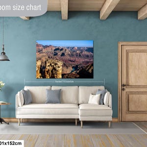 May include: A rectangular wall art print featuring a landscape photograph of the Grand Canyon, displayed above a cream-colored sectional sofa. The print measures 40 by 60 inches and shows deep red rock formations under a clear blue sky.