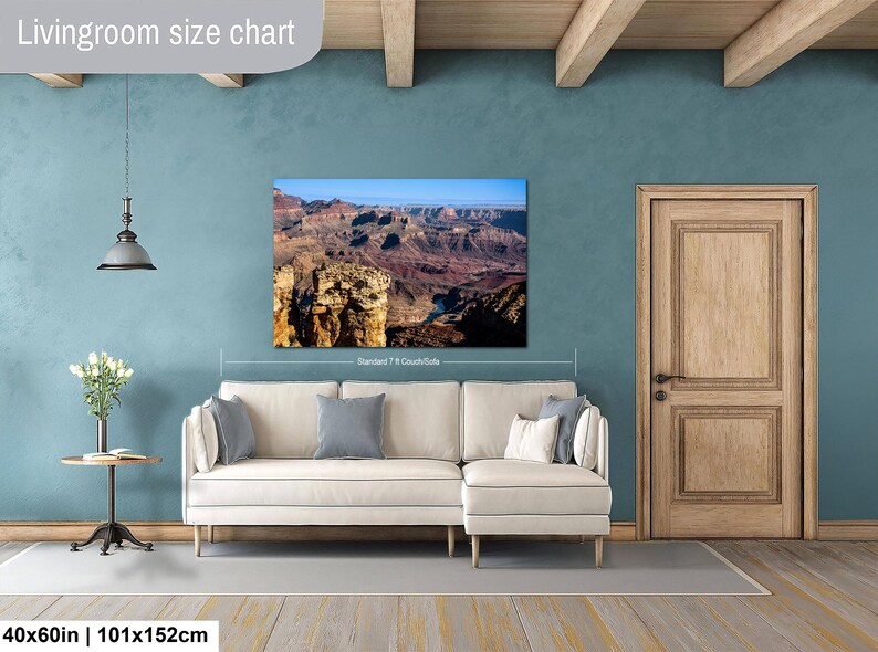 May include: A rectangular wall art print featuring a landscape photograph of the Grand Canyon, displayed above a cream-colored sectional sofa. The print measures 40 by 60 inches and shows deep red rock formations under a clear blue sky.