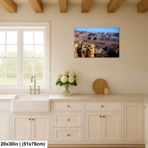 May include: A rectangular wall art print featuring a landscape photograph of the Grand Canyon with layered red rock formations, deep shadows, and a blue sky, measuring 20 inches by 30 inches, displayed above a kitchen counter.