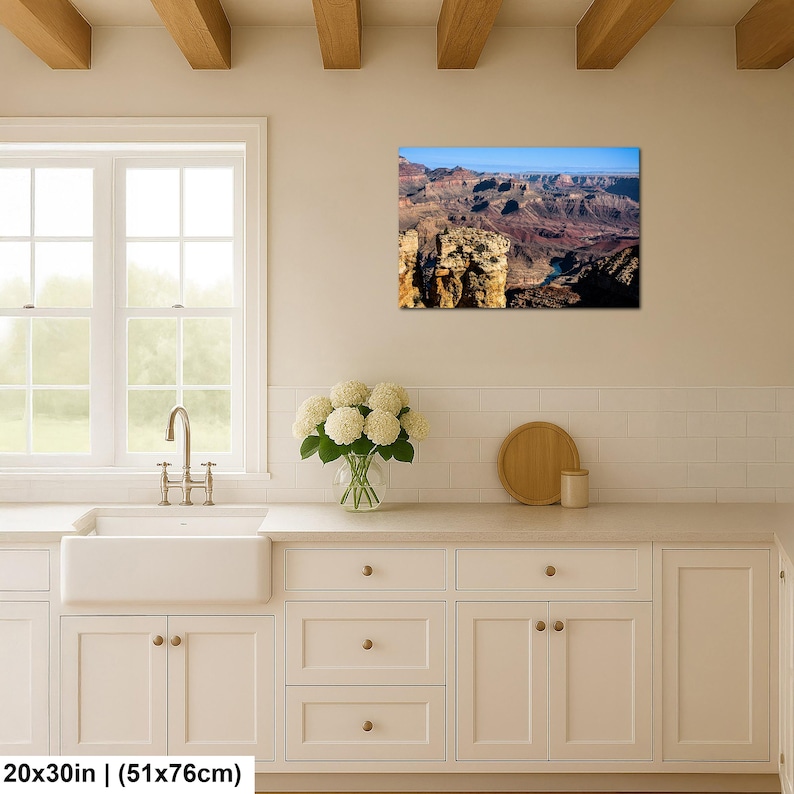 May include: A rectangular wall art print featuring a landscape photograph of the Grand Canyon with layered red rock formations, deep shadows, and a blue sky, measuring 20 inches by 30 inches, displayed above a kitchen counter.