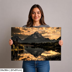 Puede incluir: Una impresi&oacute;n de arte mural rectangular de 61 por 91 cm que muestra un paisaje de monta&ntilde;a reflejado en un lago tranquilo al atardecer. La escena presenta nubes doradas, siluetas oscuras de &aacute;rboles y picos cubiertos de nieve.