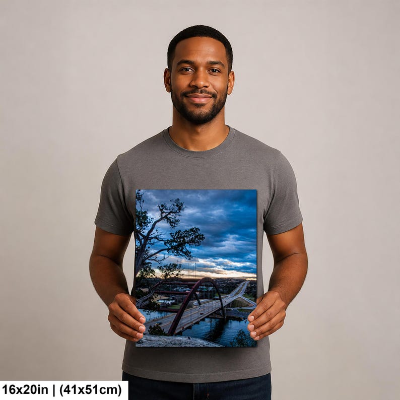 May include: A rectangular canvas print measuring 16x20 inches featuring a landscape photograph of a red arched bridge spanning a river under a dramatic, cloudy blue sky at dusk, with silhouetted trees in the foreground and a road visible.