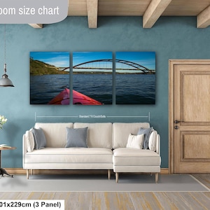 May include: A three-panel canvas wall art set depicting a red kayak on a lake facing a large arched bridge under a blue sky. The artwork is displayed above a cream-colored sectional sofa. The text Livingroom size chart and 40x90in | 101x229cm (3 Panel) is visible.