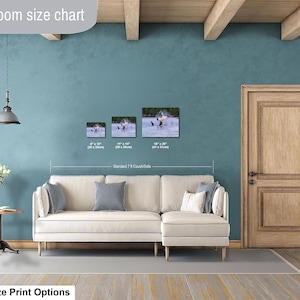 May include: A living room size chart displaying three rectangular wall art prints featuring a bird in water, labeled with dimensions 8x10 inches, 11x14 inches, and 16x20 inches, positioned above a cream-colored sectional sofa with gray accent pillows.