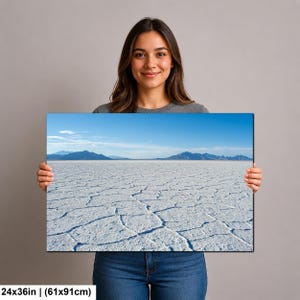 May include: A rectangular wall art print measuring 24x36 inches, featuring a landscape photograph of the Bonneville Salt Flats. The image displays a vast, white, cracked salt crust surface under a clear blue sky with distant dark blue mountains.