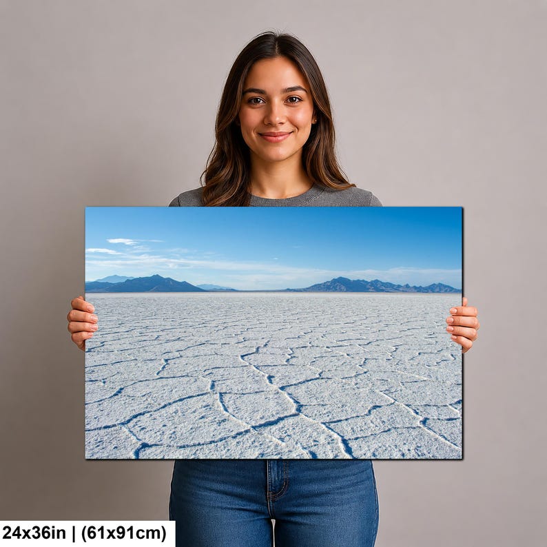 May include: A rectangular wall art print measuring 24x36 inches, featuring a landscape photograph of the Bonneville Salt Flats. The image displays a vast, white, cracked salt crust surface under a clear blue sky with distant dark blue mountains.