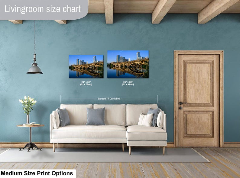 May include: A living room size chart displaying two rectangular wall art prints of a city bridge over water, labeled 20 x 30 inches and 24 x 36 inches, positioned above a cream-colored sectional sofa with gray pillows and a small side table.