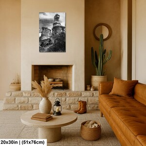 May include: A black and white wall art print featuring a tall, weathered rock formation under a cloudy sky. The rectangular print measures 20 by 30 inches and is displayed on a light-colored wall above a fireplace, showcasing natural textures.
