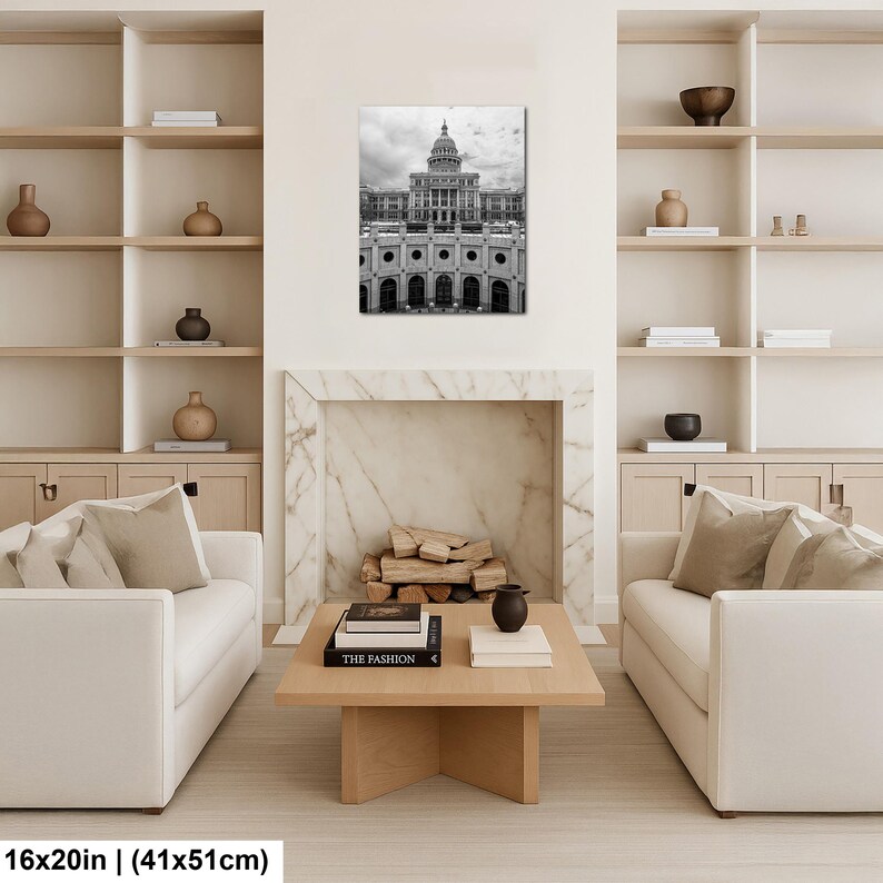 May include: A black and white wall art print featuring the Texas State Capitol building, displayed in a living room setting. The artwork measures 16 inches by 20 inches and is positioned above a fireplace mantel between two white bookshelves.
