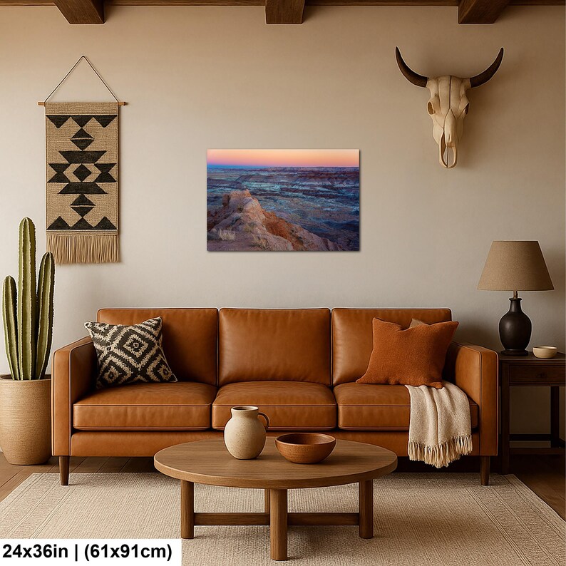 May include: A rectangular wall art print featuring a desert landscape at sunset with orange and blue hues, displayed in a living room setting. The print measures 24 by 36 inches and depicts rocky terrain under a gradient sky.