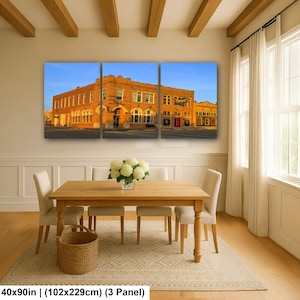 May include: A three-panel wall art set depicting a historic orange brick building under a clear blue sky. The artwork measures 40 by 90 inches in total. The scene features arched windows and architectural details of a multi-story commercial structure.