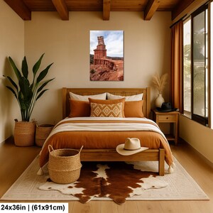 May include: A rectangular wall art print measuring 24 by 36 inches, featuring a vertical landscape photograph of a tall, weathered red rock formation set against a cloudy sky, displayed in a bedroom with a wooden bed frame and bedding.