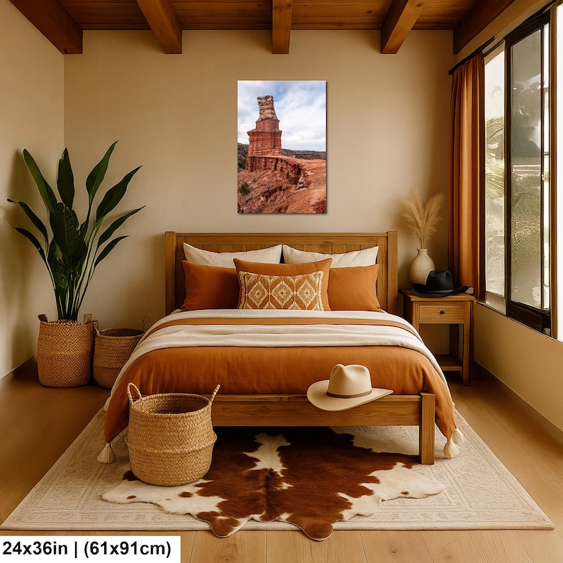 May include: A rectangular wall art print measuring 24 by 36 inches, featuring a vertical landscape photograph of a tall, weathered red rock formation set against a cloudy sky, displayed in a bedroom with a wooden bed frame and bedding.
