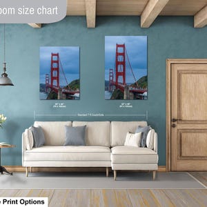 May include: A living room size chart displaying two vertical wall art prints of the Golden Gate Bridge in red, positioned above a cream-colored sectional sofa. The prints are labeled with dimensions of 30 by 40 inches and 32 by 48 inches.