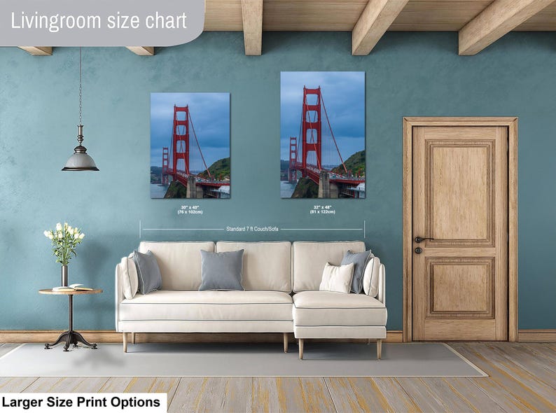 May include: A living room size chart displaying two vertical wall art prints of the Golden Gate Bridge in red, positioned above a cream-colored sectional sofa. The prints are labeled with dimensions of 30 by 40 inches and 32 by 48 inches.