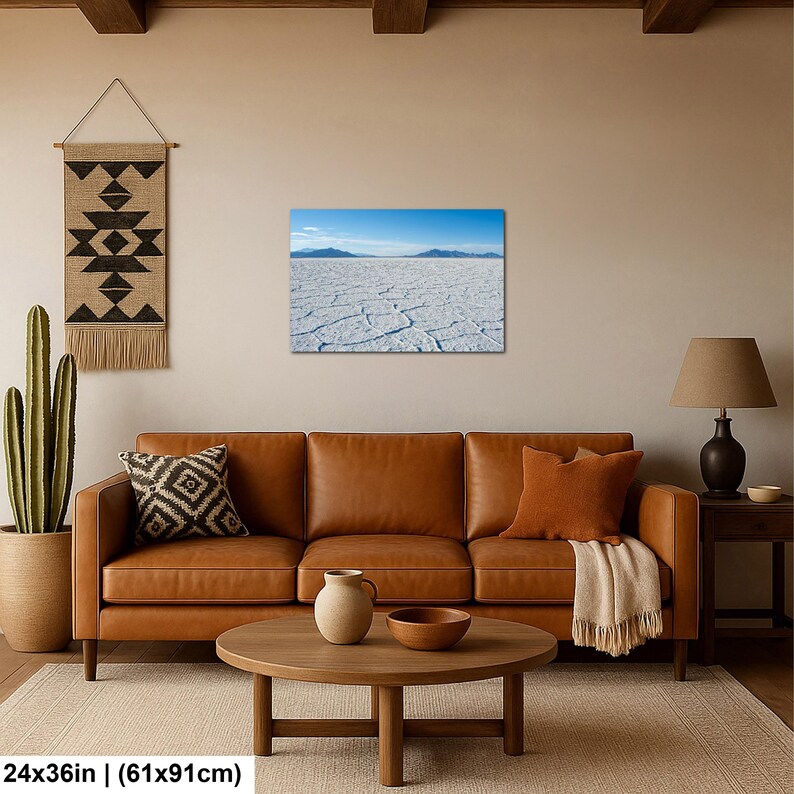 May include: A rectangular wall art print measuring 24 by 36 inches, featuring a landscape photograph of a vast, white, cracked salt flat under a clear blue sky with distant mountains on the horizon, displayed in a living room setting.