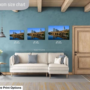 May include: A living room size chart displaying three rectangular wall art prints of a city skyline and bridge over water. The prints are labeled with dimensions 16" x 24", 20" x 30", and 24" x 36" above a standard 7 ft couch sofa.