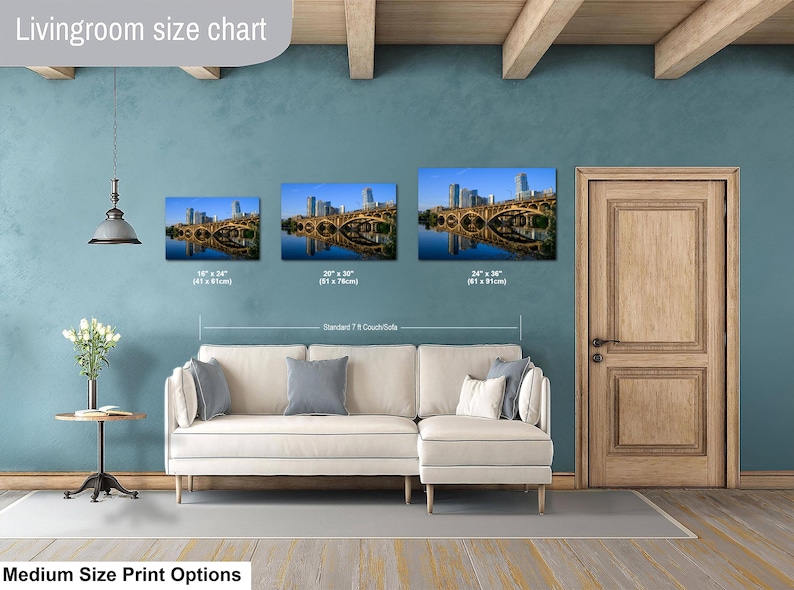 May include: A living room size chart displaying three rectangular wall art prints of a city skyline and bridge over water. The prints are labeled with dimensions 16" x 24", 20" x 30", and 24" x 36" above a standard 7 ft couch sofa.