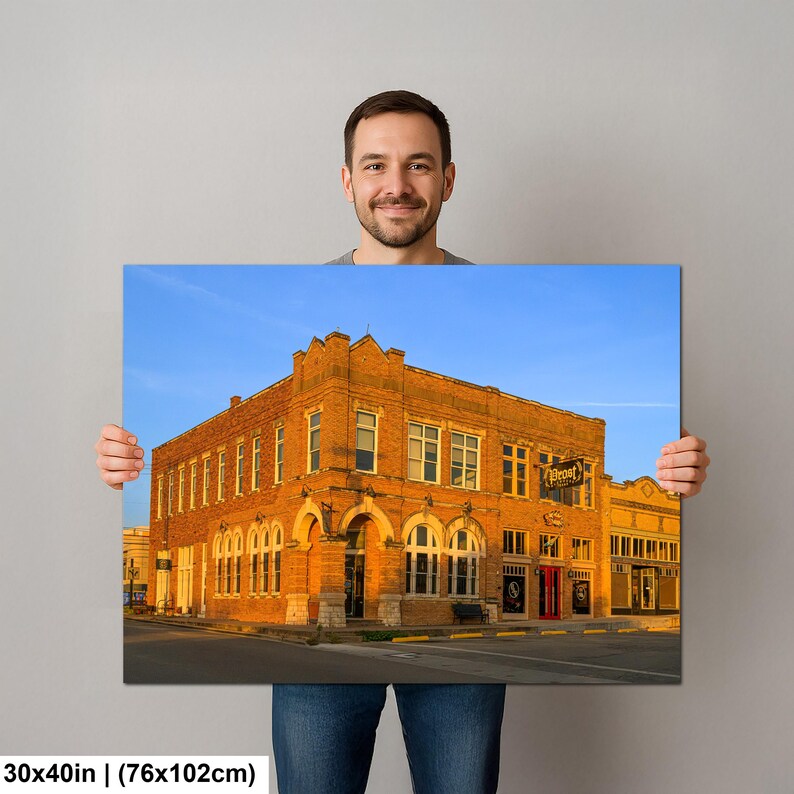 May include: A rectangular wall art print measuring 30 by 40 inches, featuring a photograph of a multi-story orange brick building at sunset. The structure has arched windows, a corner entrance, and a sign reading Prost on the exterior wall.