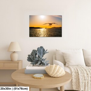 May include: A rectangular wall art print featuring a seagull in flight over a body of water during a golden sunset. The scene includes a distant shoreline and a small boat silhouette. The print measures 20 inches by 30 inches as indicated.