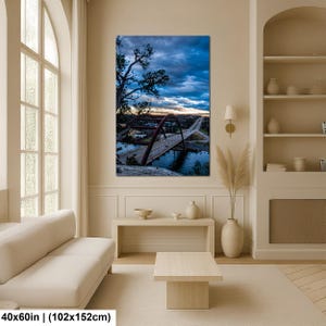 May include: A vertical wall art print featuring a landscape photograph of a red arched bridge spanning a river at twilight. The scene includes a dark blue cloudy sky, silhouetted trees in the foreground, and a road extending into the distance. 40x60 inches.