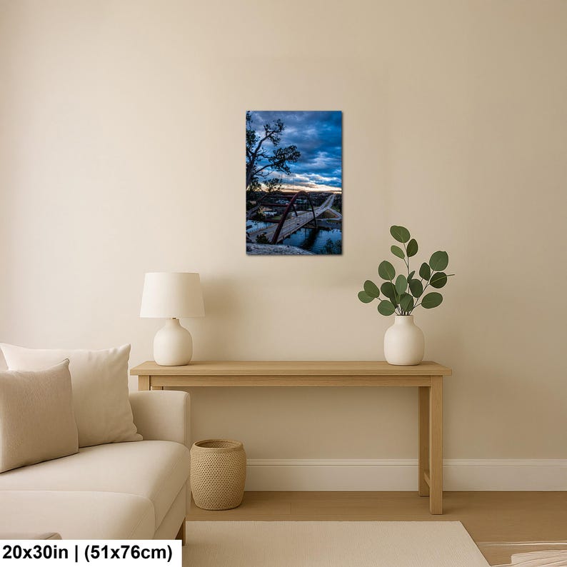 May include: A rectangular wall art print featuring a landscape photograph of a red arched bridge spanning a river at dusk. The sky is filled with dark blue and grey clouds with a hint of orange light on the horizon. The print measures 20x30 inches.