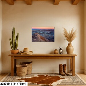May include: A rectangular landscape wall art print featuring a desert canyon at sunset with orange, pink, and blue hues. The print measures 20 by 30 inches and is displayed on a beige wall above a wooden console table with decor items.