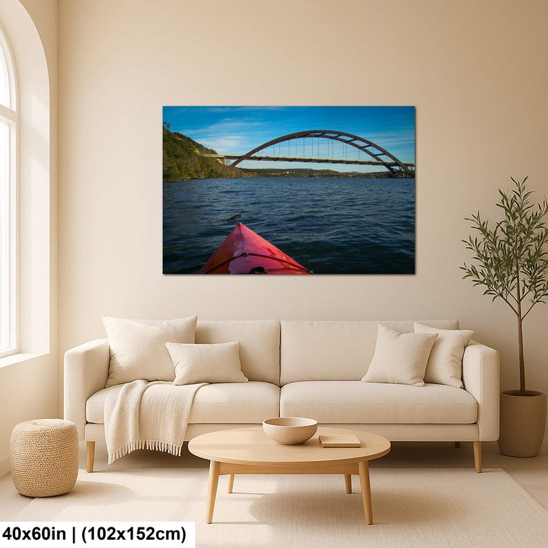 May include: A rectangular wall art print featuring a landscape photograph of a red kayak bow on dark blue water, looking toward a large arched bridge under a bright blue sky. The print measures 40 inches by 60 inches and is displayed on a wall.