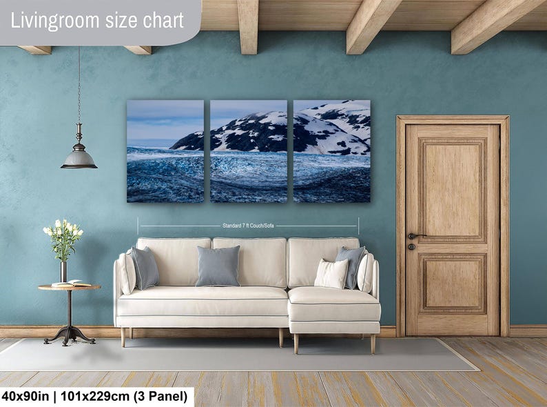 May include: A three-panel wall art set depicting a snowy mountain landscape with dark blue water, displayed above a cream-colored sectional sofa. The text "Livingroom size chart" and "40x90in | 101x229cm (3 Panel)" is visible on the image.