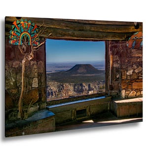 Könnte beinhalten: Ein rechteckiger Wandkunstdruck, der einen Innenraum mit Steinwänden zeigt, mit Blick durch ein großes Fenster auf einen entfernten Tafelberg. Die Szene umfasst einen dekorativen, bunten geometrischen Wandbehang und einen knorrigen Ast.