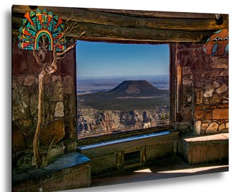 Puede incluir: Un cuadro rectangular que muestra un interior de paredes de piedra con una gran ventana que da a una montaña lejana de cima plana. La escena incluye un adorno de pared geométrico y colorido y una rama de madera nudosa.