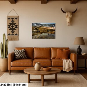 K&ouml;nnte beinhalten: Ein rechteckiger Wandkunstdruck mit den Ma&szlig;en 61 x 91 cm, der eine Landschaftsaufnahme eines geothermischen Gebiets mit dampfenden Becken, mineralreichen orangefarbenen und braunen Terrassen und fernen Bergen unter blauem Himmel zeigt.