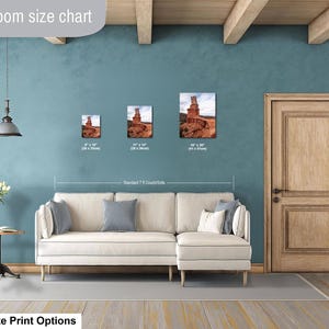 May include: A living room size chart displaying three framed landscape prints of a desert rock formation above a cream-colored sectional sofa. The prints are labeled with dimensions of 8x10 inches, 11x14 inches, and 16x20 inches for size comparison.